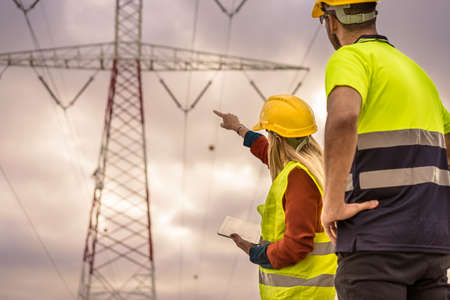 Picture of two electrical engineers using a tablet standing at a High-voltage tower to view the planning work by producing electrical energy at high voltage electrodes.の写真素材