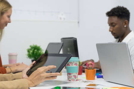 Full concentration at work. Group of young business people working while sitting at the office desk together. Hands woman teacher or tutor with adult students in classroom at desk with black tablet. Job and study concept.の写真素材