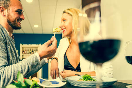 Portrait of attractive, cute, sweet, lovely, festive, cheerful couple. Man feeding his woman, giving food with fork, having fun. Food and love concept.の写真素材