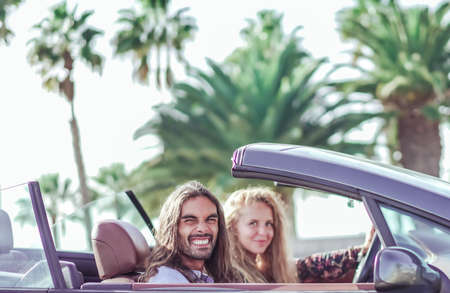 Freedom of the open road. Side view of joyful young man relaxing on the front seat while his girlfriend sitting near and driving their convertible. Transport and holiday concept.の写真素材