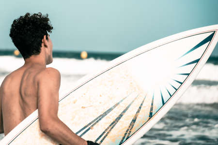 Closeup shot of a surfer holding a surfboard at the beach. A surfer with his surfboard looking to the waves. Sport and holiday concept.の写真素材