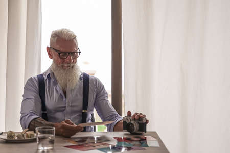 Experienced senior photographer with his old camera in the studio looking old pictures. Pensioner concept.の写真素材