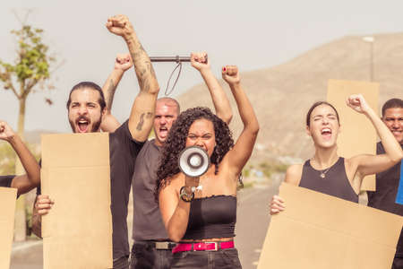 Young people demonstrate against the mandatory vaccination. Arms raised in protest. Group of protestors fists raised up in the air. Racism, coronavirus, anti vax, equality and gay pride concept. Copy space in banners.の写真素材