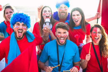 Football supporter fans friends cheering to soccer cup match at interneational stadium. Young people group with red and blue t-shirts having excited fun. European, world, champions and league concept.の写真素材