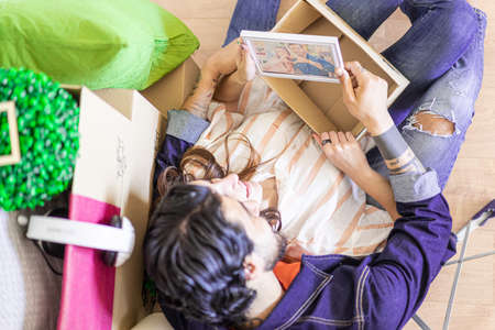 Happy young couple looking the old photo. Man and woman sitting near carton boxes in new property house. Rent, Buy, lifestyle and relationship concept.の写真素材
