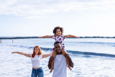 Multiracial family having fun at the beach. Father and mother and daughter playing together outdoor on beach. Holiday and travel concept.の写真素材