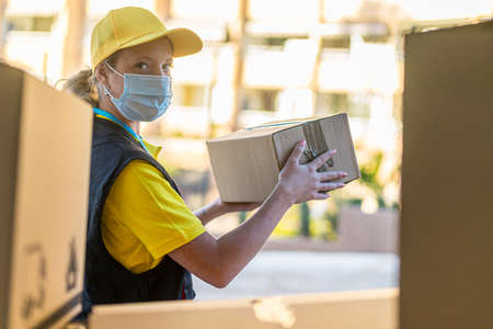 Health protection, safety and pandemic concept delivery woman in face protective medical mask holding parcel box.の写真素材