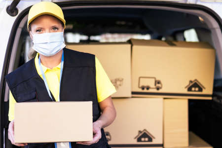 Health protection, safety and pandemic concept delivery woman in face protective medical mask holding parcel box. Copy space on the box.の写真素材