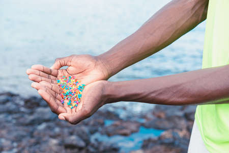 Hands full of microplastics on the beach. Different plastic colored ... Plastic pollution concept.の写真素材