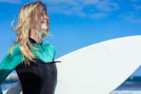 Young sexy girl with long blonde hairs, smiling and jogging with surf board on the beach in a summer day. Blue sky background. Copy space.の写真素材