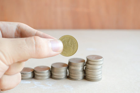 hand and Coins of Thailand on wooden floor
