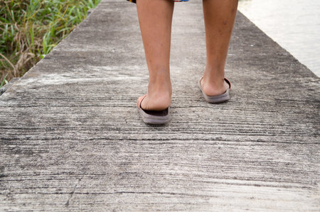 The legs and feet of a young boy standing on a cement floor