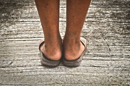 The legs and feet of a young boy standing on a cement floor