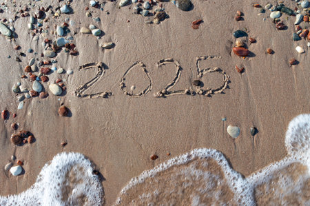 Message Year 2024 replaced by 2025 text written on beach sand background. Good bye 2024 hello to...