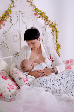 Breastfeeding baby. Young mother holding her newborn child. Mom nursing baby. Woman and new born boy in white bedroom. Family at homeの写真素材