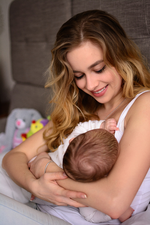 Breastfeeding baby. Pretty mother holding her newborn child. Mom smile and nursing infant. Beautiful woman and new born love at home. BlondÐµ mother breast feeding baby.の写真素材