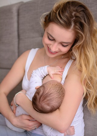 Breastfeeding baby. Pretty mother holding her newborn child. Mom smile and nursing infant. Beautiful woman and new born love at home. BlondÐµ mother breast feeding baby.の写真素材