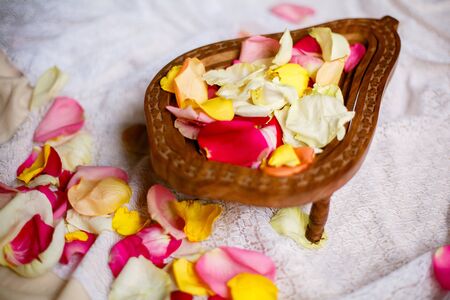 brown wooden bowl with red yellow pink rose petals on a white clothの写真素材