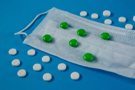 medical mask on the face and white and green pills, on a blue background side view