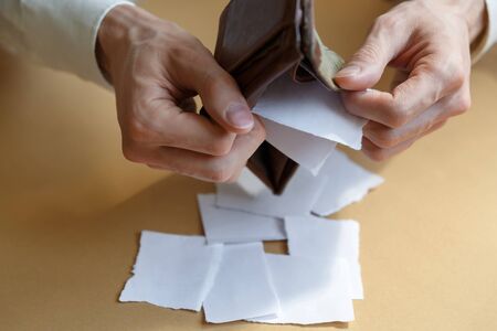 Side view of a man shaking pieces of paper from an empty wallet on a light monophonic background....