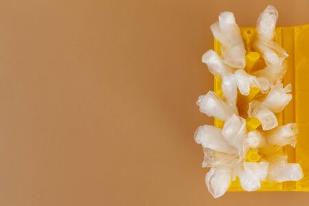transparent plastic bags in a yellow plastic egg container on a brown background. Ecology and trash