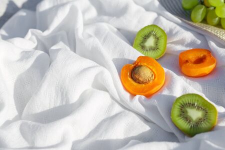 Still life and food photo. Kiwi and apricot fruit lie on a white wave-crumpled fabric under bright...