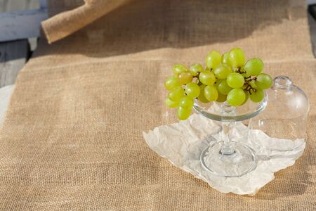 Still life and food photo. A dish with a bunch of green grapes in the footed service plate and mini dome stands on a burlapの写真素材