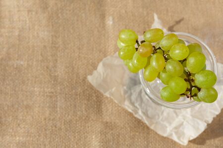 Flat lay, still life and food photo. A dish with a bunch of berries of green grapes stands on a burlapの写真素材