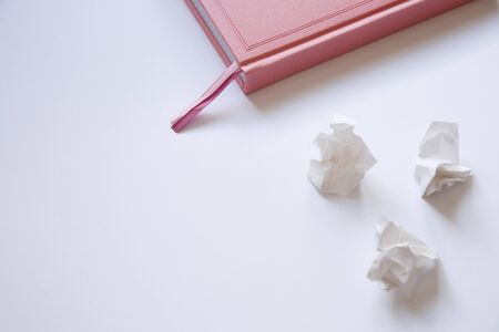 Pink diary on a white background and crumpled pieces of paper. Mistakes in the letterの写真素材