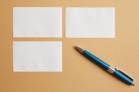 White sheets of paper for notes on a brown paper background and a blue metal pen flat layの写真素材