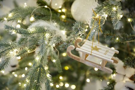 Christmas toy sled hanging on a branch of spruce. New year tree decorated with a garlandの写真素材