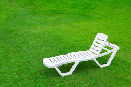 Recreation and tourism advertising. Empty white plastic chair or chaise longue, on the green grass of a fresh lawn. Place for textの写真素材