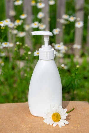 white cosmetic bottle for soap or shampoo on wooden shelf with chamomile background.の写真素材