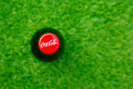 red cap on a bottle of soda coke, against a background of green grass or lawn. Place for text.のeditorial素材