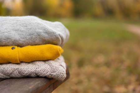 stack of knitted clothes on wooden bench in park. Autumn Warm Woolen Sweater.の写真素材