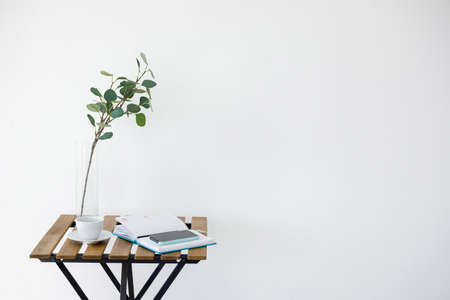 Wooden table against background of white wall. Vase with eucalyptus branch, white cup and smartphone...