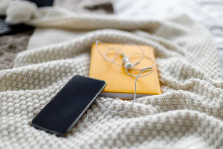 smartphone and white headphones lie on yellow notepad. Gray knitted background. Home study. Distance educationの写真素材