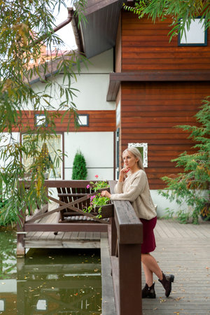 Young beautiful blonde woman in sweater stands by pond and looks sadly to side. Copy space and place for textの写真素材