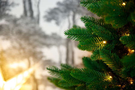 New Year and Christmas background. Artificial Christmas tree decorated with a garland, against the background of a blurred gray wall. Place text or product, copy spaceの写真素材