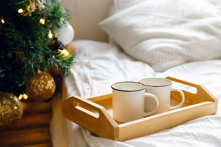 wooden tray and two white mugs on the bed on a white sheet, near a decorated Christmas tree. Cozy morning. Coffee in bedの写真素材