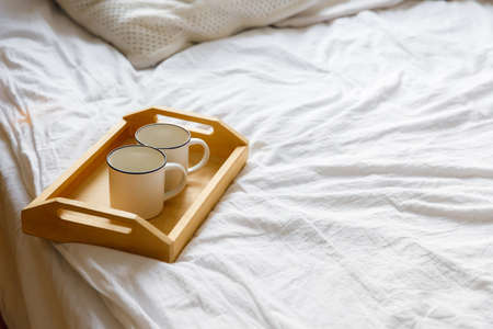 wooden tray and two white mugs on the bed on a white sheet. Cozy morning. Coffee in bedの写真素材