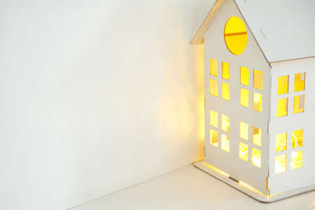 white wooden house with yellow light from the windows, on a white background. Home comfort concept. Mortgage and rental of apartments