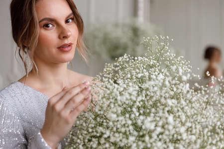 portrait of beautiful woman in silver evening dress with sequins. Glamor and beautiful life. Young woman holds bouquet of white gypsophila flowers in her hands. Bride at wedding, wife. bridal bouquetの写真素材
