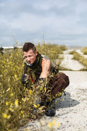 male vandal in dirty clothes hiding in the grass on an abandoned bridge