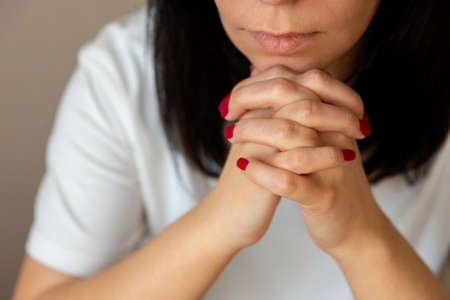 woman put her chin on her crossed fingers and prays.