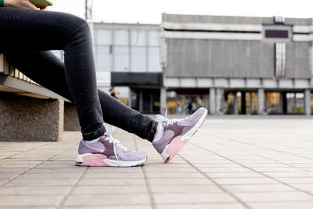 woman in black jeans and sneakers sits on bench. Women's legs in pink sneakers close upの写真素材