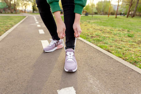 woman in sneakers stands on the path and ties her shoelaces. Women's legs in pink sneakers close up