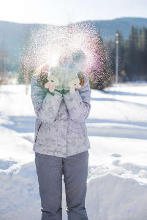 girl stands on street and blows on snow. Young woman stands in winter field in warm jacket and pants