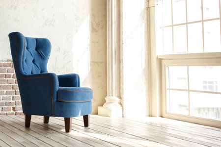 blue armchair stands on wooden floor, against background of wall with an antique style column and large windowの写真素材