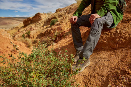 man tourist in membrane jacket, tactical pants and hiking boots sits in sand career. Sights of...